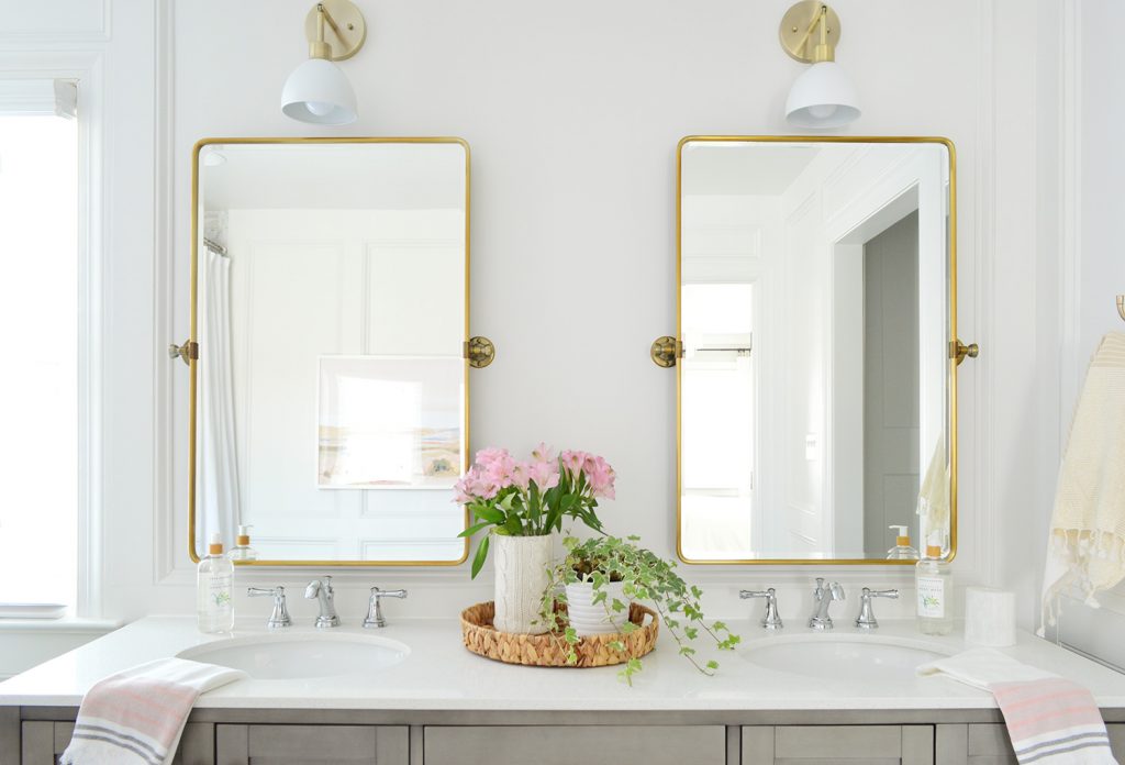 Two gold pivot mirrors over gray bathroom double vanity