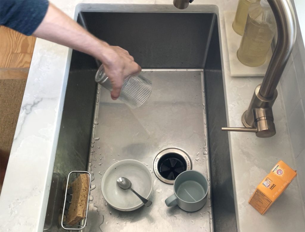 Hand removing dirty glass from dirty stainless steel sink for cleaning