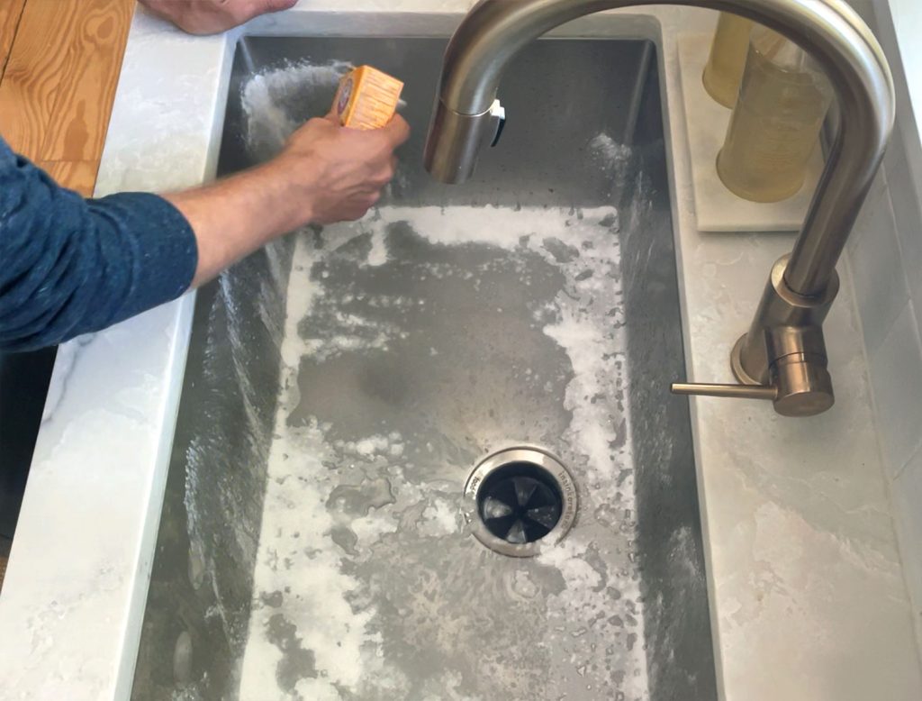 Hand sprinkling baking soda around stainless steel sink to be cleaned