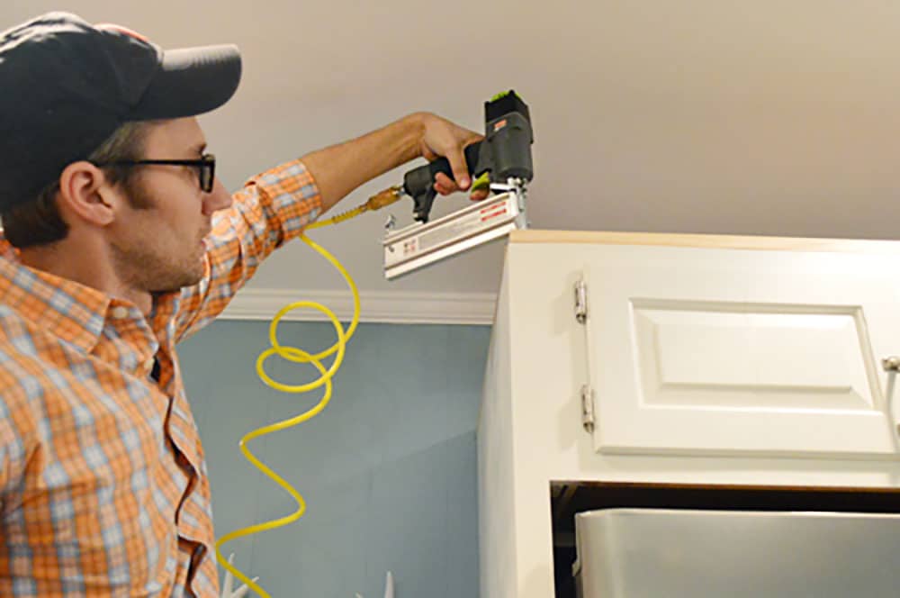 John using nail gun to attached scrap wood to top of cabinet