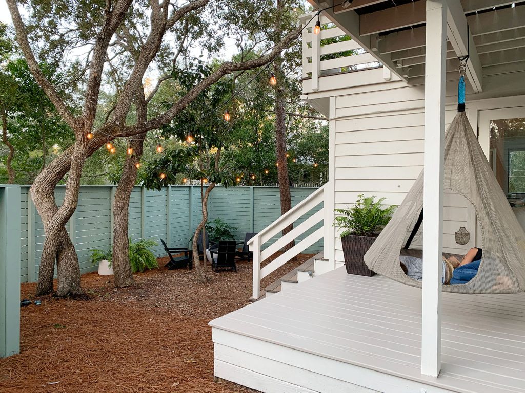 Two kids laying in hanging tent on covered porch with green painted fence in background